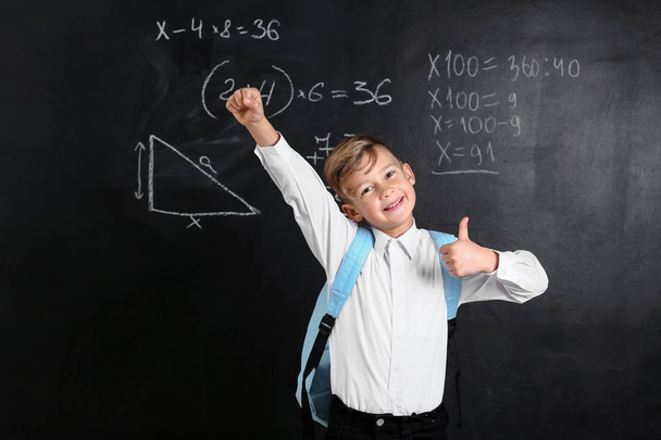 Cute little schoolboy with backpack showing thumb-up near blackboard - Photo, Image