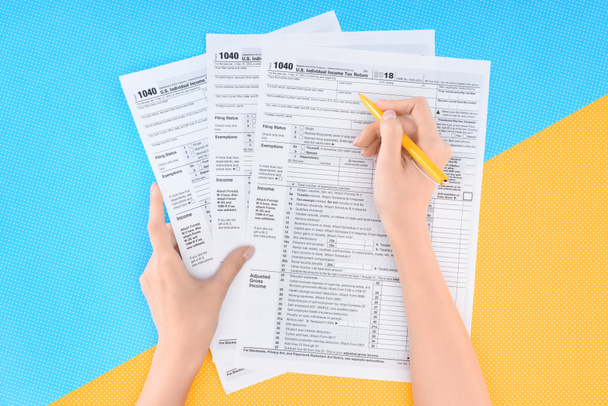 Teilansicht der Frau beim Ausfüllen von Steuerformularen auf blauem und gelbem Hintergrund - Foto, Bild
