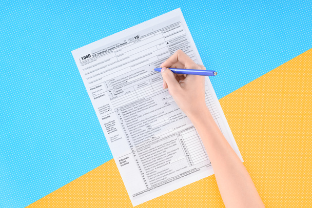 bijgesneden beeld van vrouw vullen belastingformulier op blauwe en gele achtergrond - Foto, afbeelding
