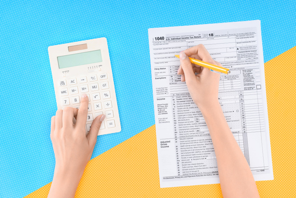 обрезанный вид женщины с помощью калькулятора и заполнение налоговой формы на синем и желтом фоне
 - Фото, изображение