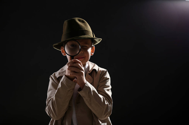 Χαριτωμένο μικρό ντετέκτιβ με μεγεθυντικό φακό σε σκούρο φόντο - Φωτογραφία, εικόνα