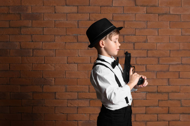 Schattige kleine detective met pistool tegen muur - Foto, afbeelding