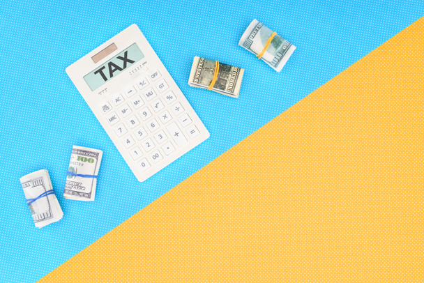 pohled shora kalkulačka s slovo "daň" a peníze vrátí na modré a žluté pozadí - Fotografie, Obrázek