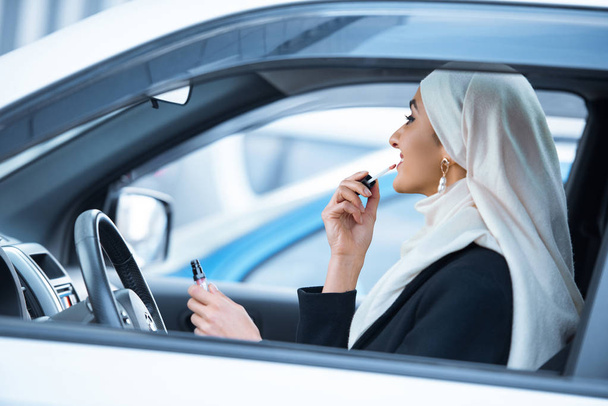 genç Müslüman kadın arabada oturan ve makyaj uygulamak - Fotoğraf, Görsel