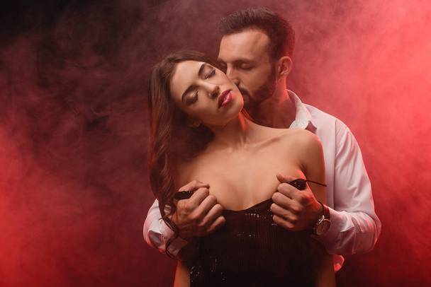 handsome passionate man undressing his girlfriend in red smoky room  - Photo, Image