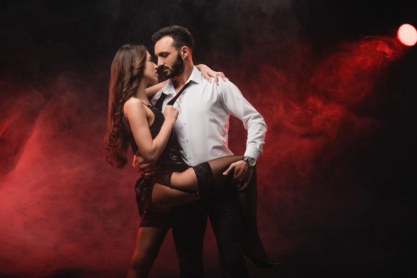 heterosexual passionate couple hugging in red smoky room  - Фото, зображення