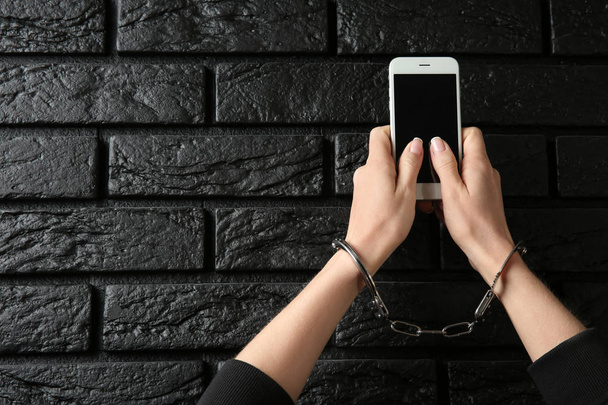 暗い背景に携帯電話で手錠をかけられて女性。中毒の概念 - 写真・画像