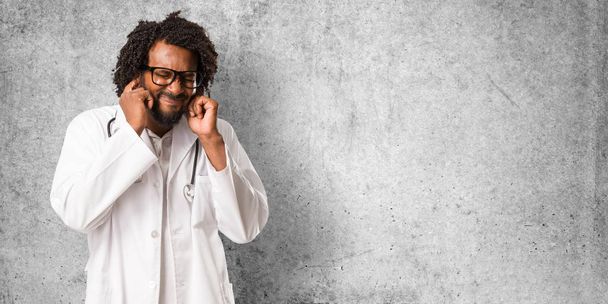 Красивый африканский американский врач, закрывающий уши руками, злой и уставший слышать какой-то звук
 - Фото, изображение