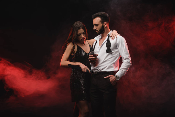 vášnivá žena objímala muž se sklenkou whisky v červené zakouřené místnosti  - Fotografie, Obrázek
