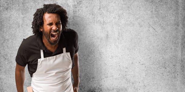 Guapo panadero afroamericano gritando enojado, expresión de locura e inestabilidad mental, boca abierta y ojos medio abiertos, concepto de locura
 - Foto, Imagen