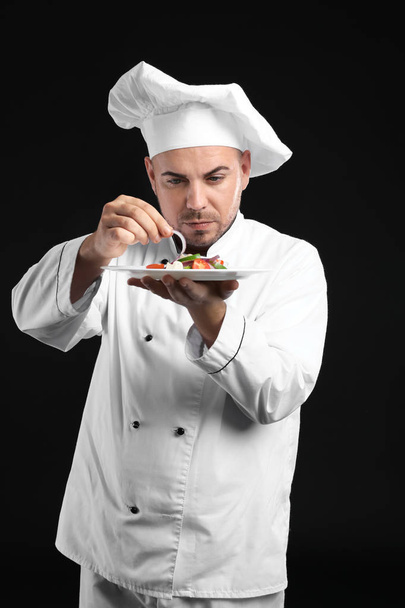 Αρσενικό σεφ με νόστιμη σαλάτα σε σκούρο φόντο - Φωτογραφία, εικόνα