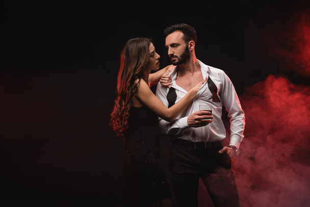 sensual girl hugging man with glass of whiskey in red smoky room  - Photo, Image