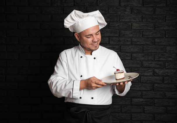 Male chef with tasty dessert on dark background - Foto, imagen