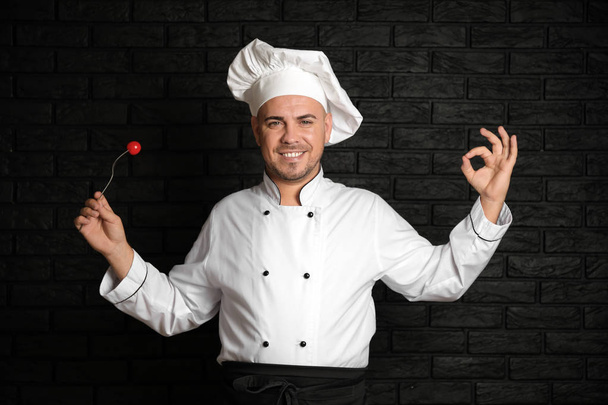 Férfi szakács paradicsom a villát mutatja az Ok gesztus sötét háttér - Fotó, kép