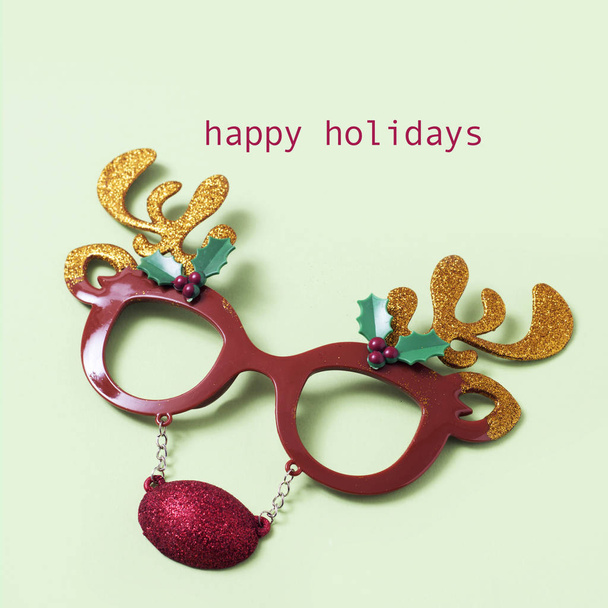 eyeglasses in the shape of a reindeer face and the text happy holidays on a pale green background - Foto, afbeelding