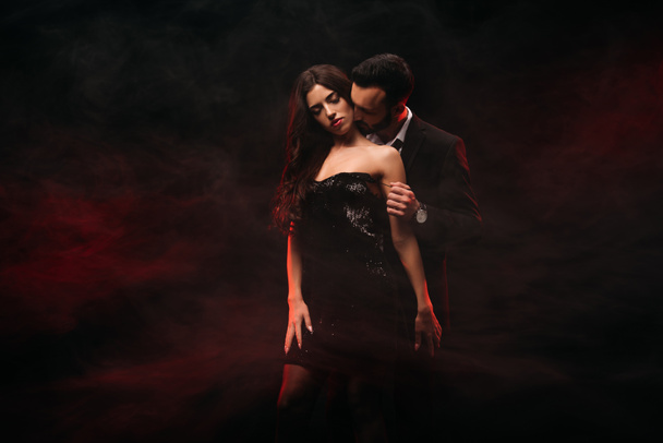 Красивый мужчина обнимает соблазнительную женщину в красной дымовой комнате
  - Фото, изображение