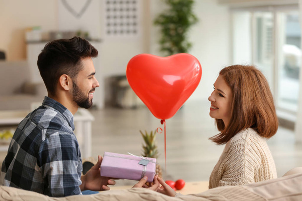 Young man giving present to his beloved girlfriend at home. Celebration of Saint Valentine's Day - Фото, изображение