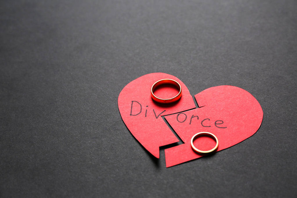 gebrochenes rotes Herz mit Ringen auf dunklem Hintergrund. Scheidungskonzept - Foto, Bild