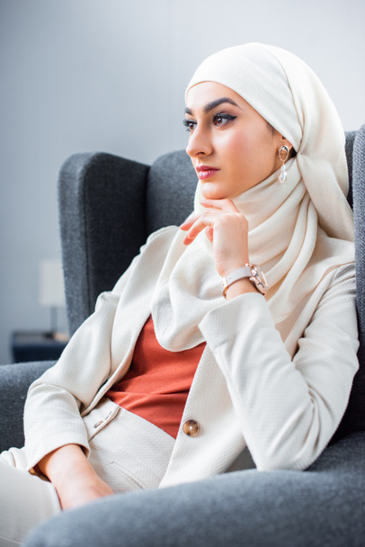 beautiful pensive young muslim woman sitting in chair and looking away   - Fotó, kép