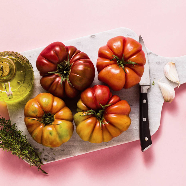 brandywine tomato on a cutting board. cooking summer salad with fresh olive oil, thyme. on a rose background - Photo, Image