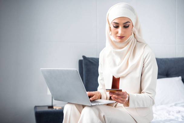 молода мусульманка тримає кредитну картку і використовує ноутбук
  - Фото, зображення