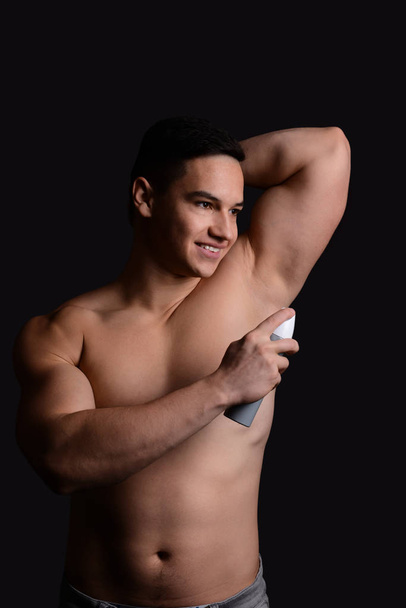Молодий чоловік використовує дезодорант на темному тлі
 - Фото, зображення