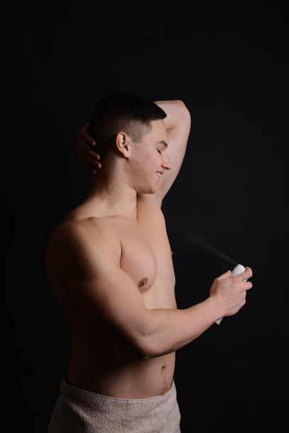 Young man using deodorant on dark background - Photo, Image