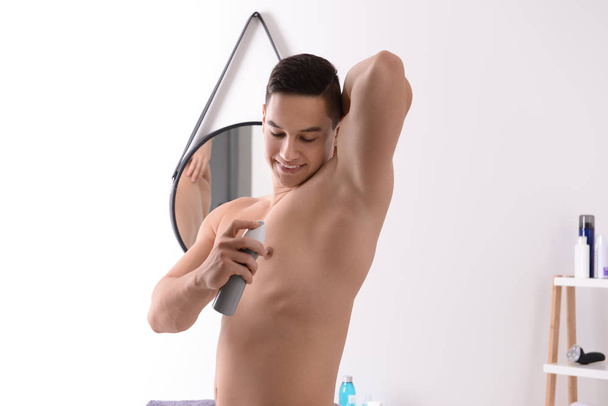 Hombre joven usando desodorante en el baño
 - Foto, Imagen