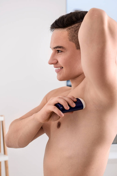 Young man using deodorant in bathroom - Foto, afbeelding