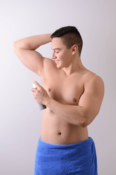 Young man using deodorant on light background - Foto, afbeelding