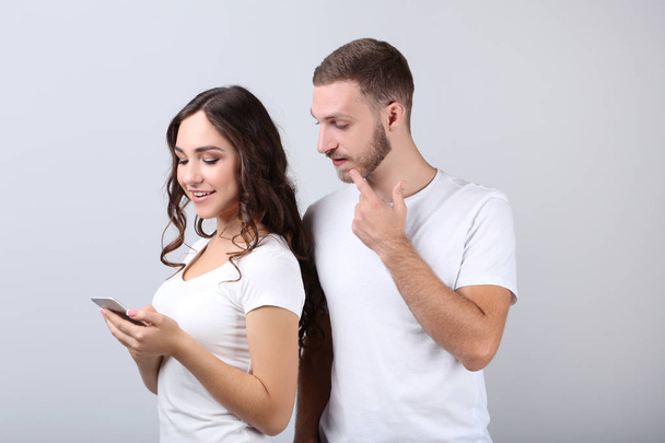 Beautiful young couple and smartphone on grey background - Foto, Imagen