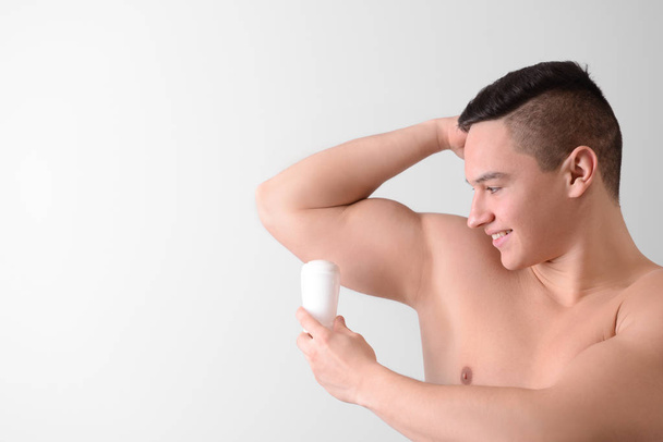 Young man with deodorant on light background - Foto, imagen