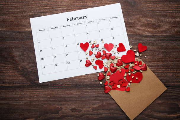 Red hearts in envelope with february calendar on wooden table - Fotó, kép