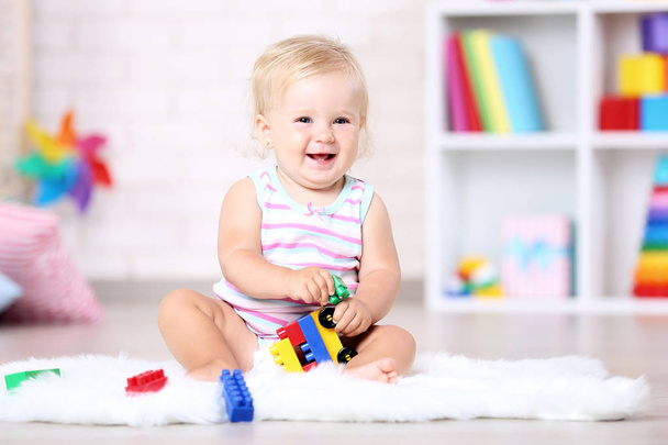 Baby girl sitting on white carpet with toys - Foto, imagen