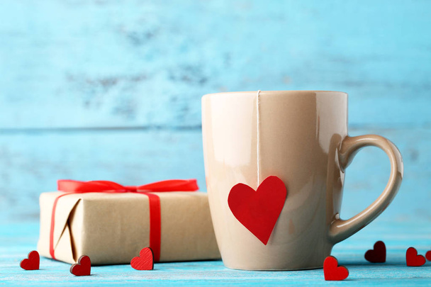 Cup of tea with red hearts and gift box on wooden table - Fotó, kép