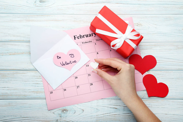Female hand holding white heart above february calendar with envelope and gift box - Foto, imagen
