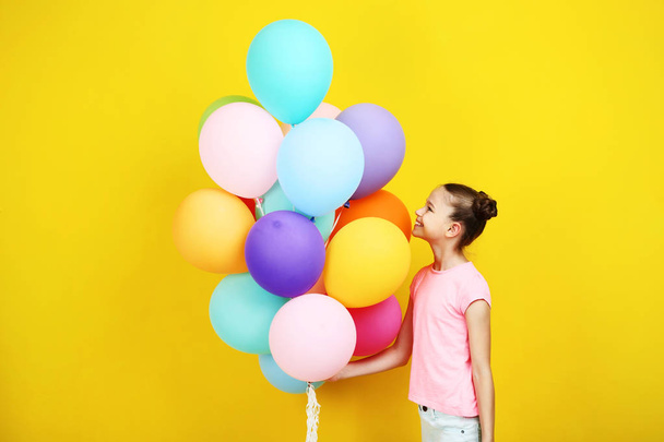 Beautiful young girl with colored balloons on yellow background - Zdjęcie, obraz