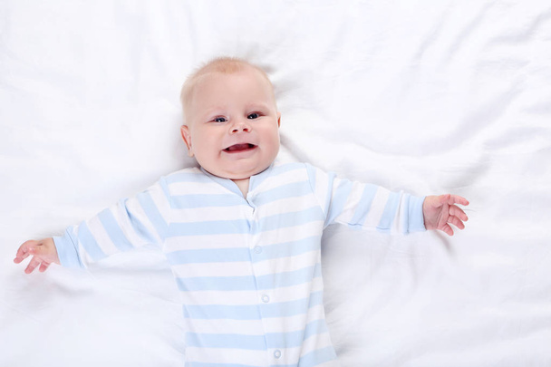 милий усміхнений хлопчик лежить на білому ліжку
 - Фото, зображення