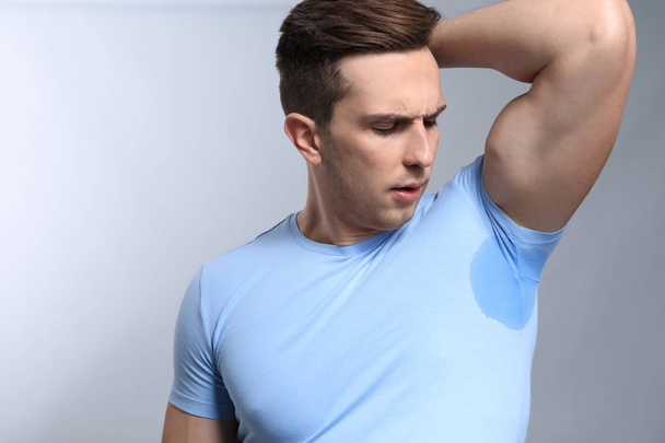 Young man with wet spot on clothes under armpit against grey background. Concept of using deodorant - Photo, Image