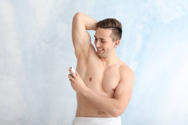 Handsome young man with deodorant on light background - Photo, Image