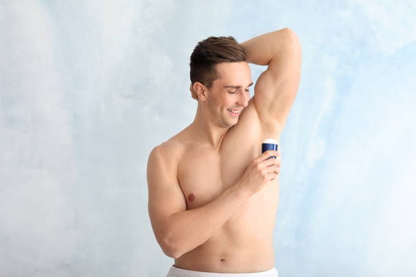 Handsome young man with deodorant on light background - Valokuva, kuva
