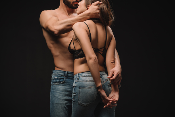 cropped view of shirtless man hugging sexy girlfriend in handcuffs isolated on black - Φωτογραφία, εικόνα