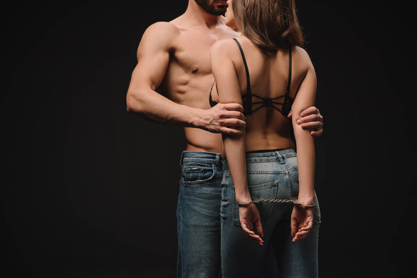 cropped view of shirtless man hugging passionate girlfriend in handcuffs isolated on black - Foto, Imagem