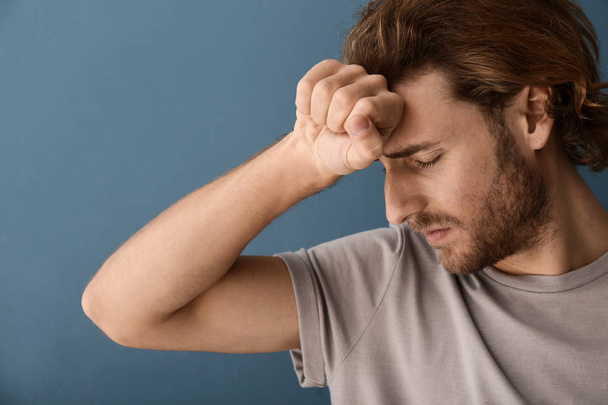 Junger Mann leidet unter Kopfschmerzen auf farbigem Hintergrund - Foto, Bild