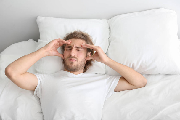 Young man suffering from headache in bedroom - Foto, imagen