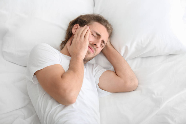 Young man suffering from headache in bedroom - Foto, Imagen
