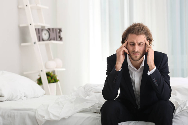 Молодой бизнесмен страдает от головной боли в спальне
 - Фото, изображение