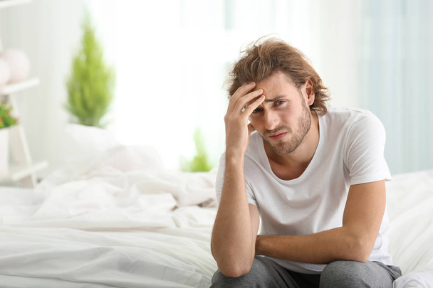 Young man suffering from headache in bedroom - Photo, Image