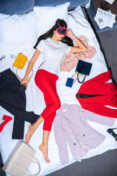 вид сверху на молодую женщину в маске для глаз спящую на кровати с кофе на вынос, паспорт и посадочный талон
 - Фото, изображение