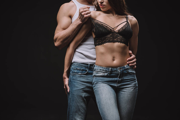 cropped view of man undressing girl in lace bra isolated on black - Фото, изображение